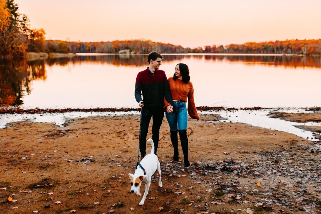 Photo of a couple walking their dog on the beach at Lincoln Woods State Park in Rhode Island for their engagement photos
