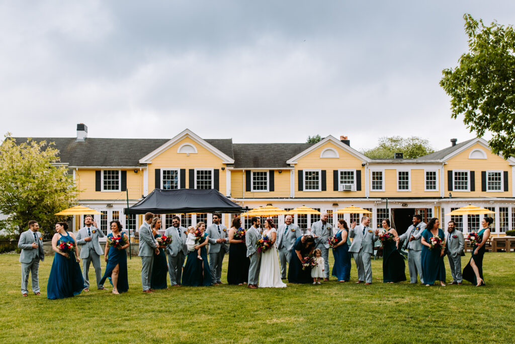 A large bridal party gathers in front of the yellow outside at Agawam Hunt in Rhode Island