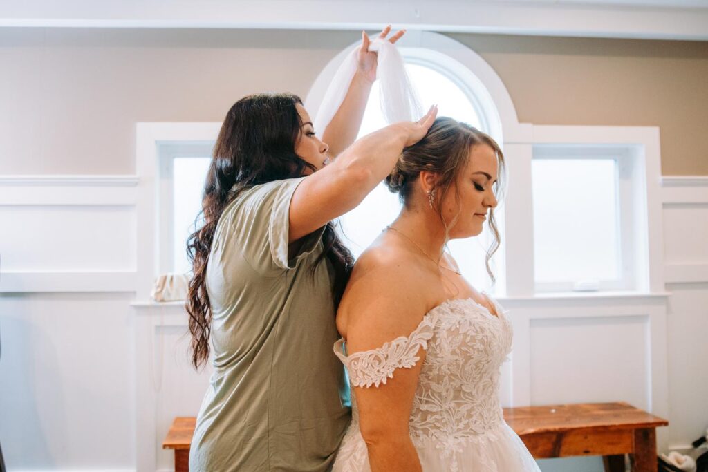 Bride smiling as her veil is placed, natural light pouring in through Birch Wood’s signature arched windows