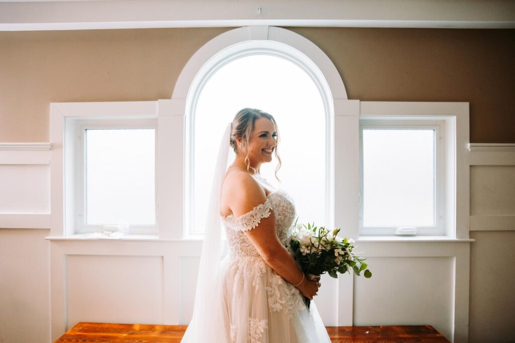 Portrait of the bride gazing out the window holding her bouquet, surrounded by soft natural light