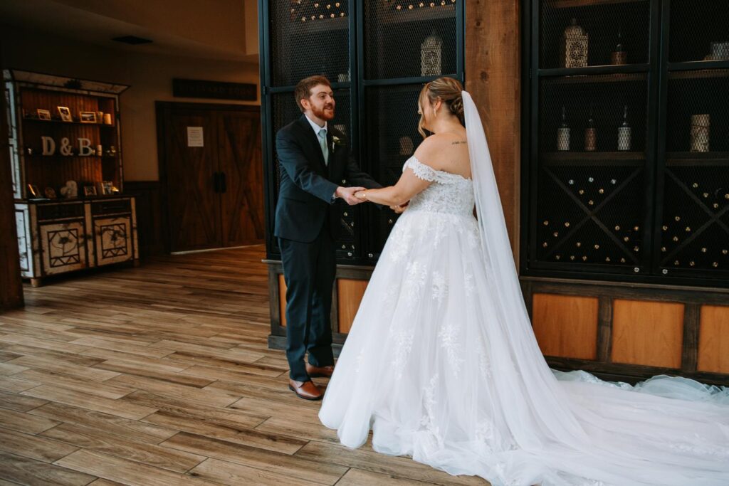 Bride and groom sharing a joyful first look in front of the wine cellar at Birch Wood Vineyards
