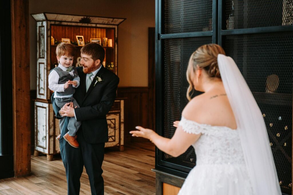 Bride and groom smiling while holding their young son before the ceremony begins