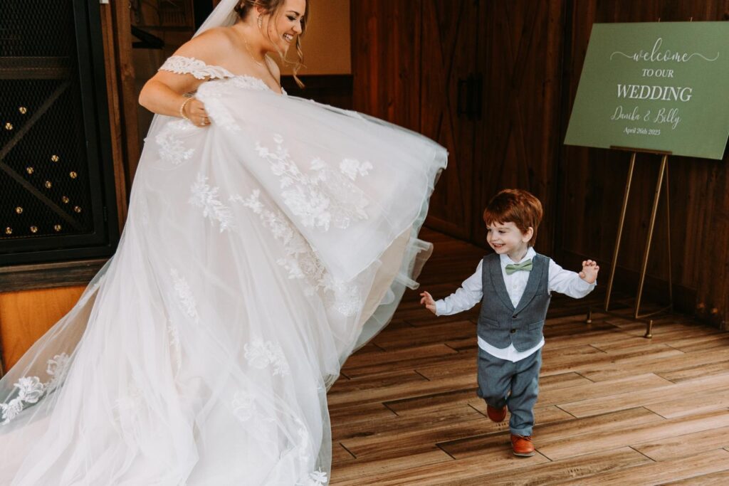 Bride twirling in her dress while holding hands with her son in front of their wedding welcome sign