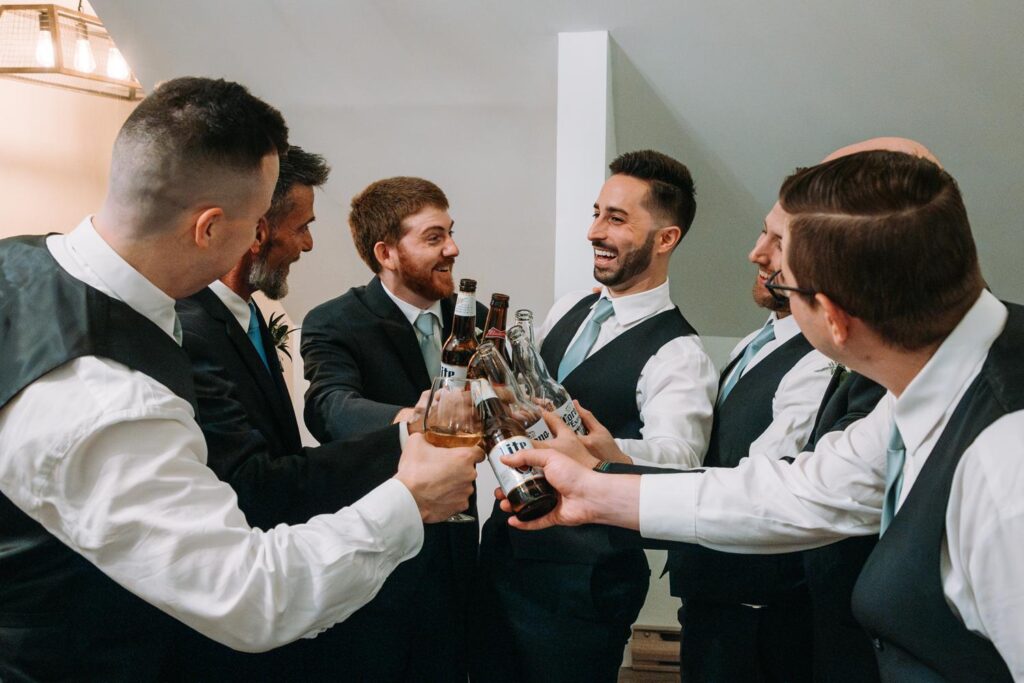 Groom and groomsmen clinking glasses during a relaxed toast before the ceremony