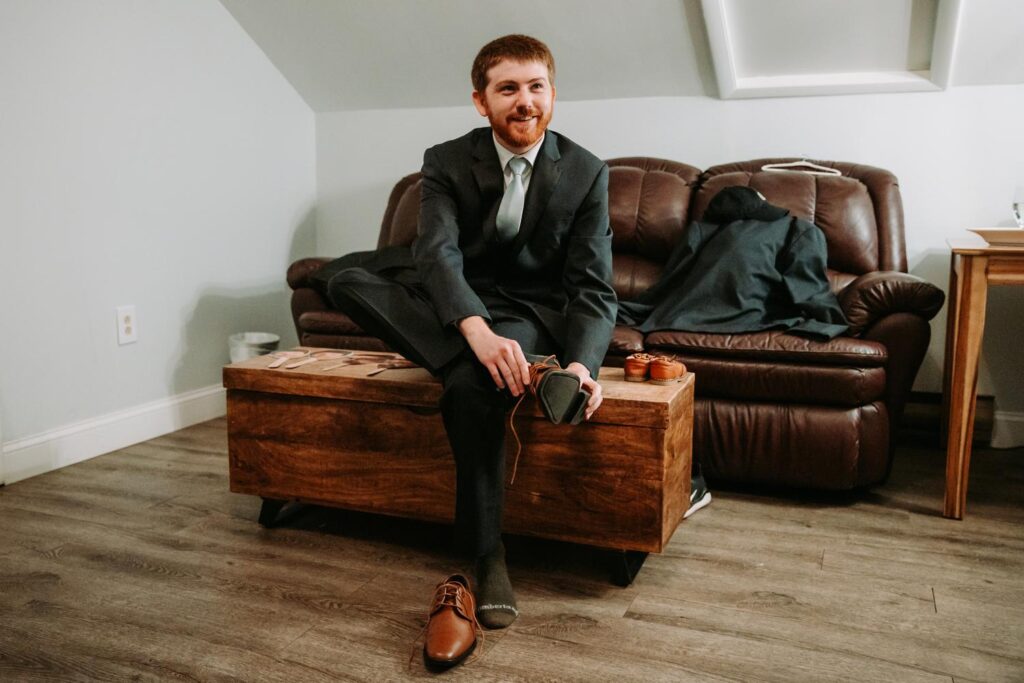 Groom sitting relaxed on a leather couch in the Birch Wood Vineyards getting ready room