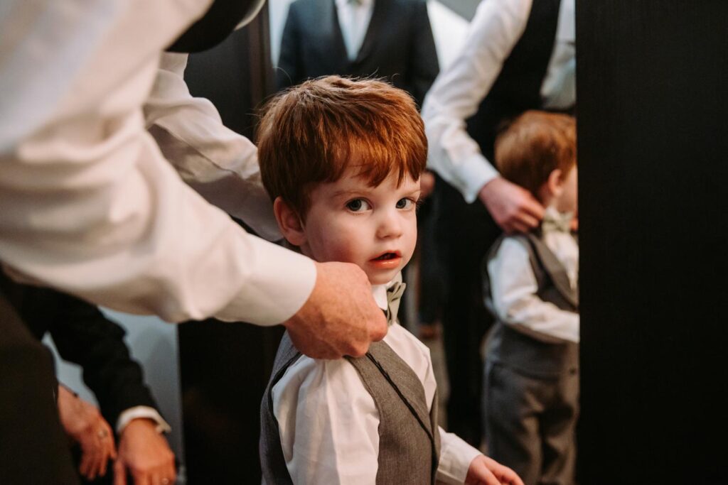 Groom helping their young son get dressed in a vest and tie before the wedding ceremony