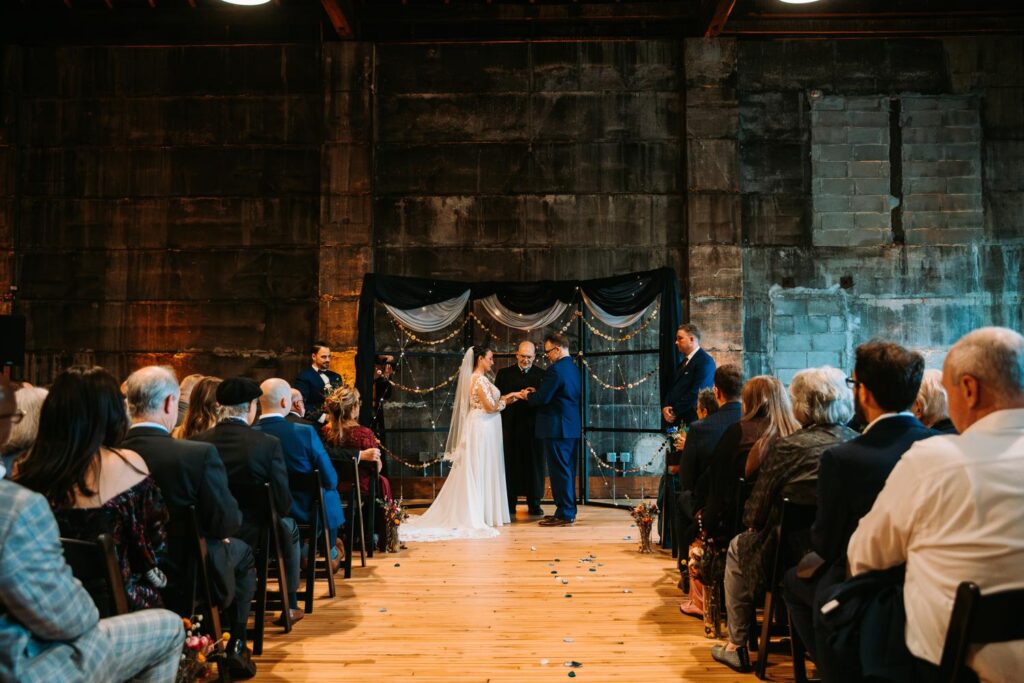 Wide shot of the wedding ceremony setup at Olio with dark stone walls and draped fabric.