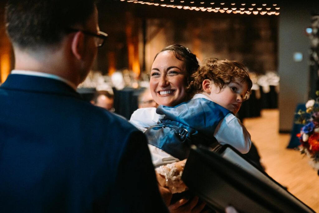 Bride holding one of the boys during ceremony vows, laughing joyfully.