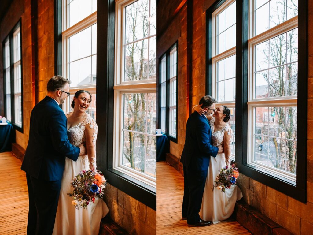 Couple cuddled together by the windows of the industrial venue with bouquet in hand.