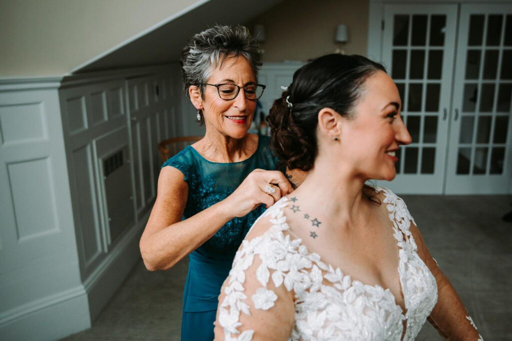 Bride’s mom helping fasten her lace wedding dress in a quiet moment.