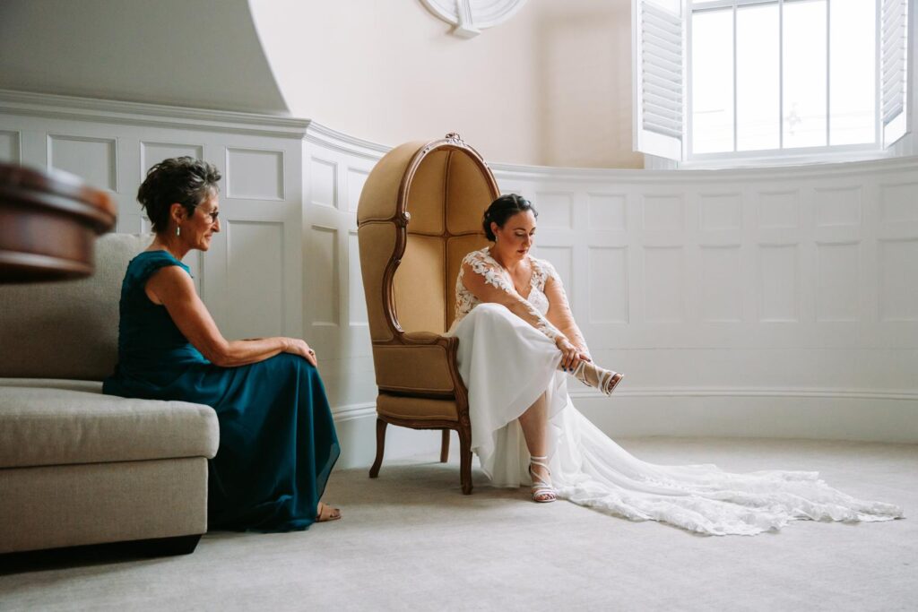 Bride putting on her shoes while chatting with her mom during a peaceful pause.