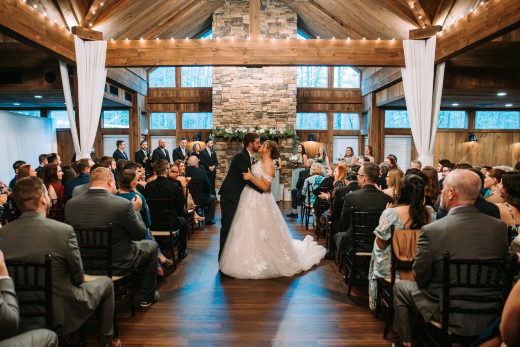 Wide-angle shot of the ceremony with guests looking on in a glowing, wood-toned room