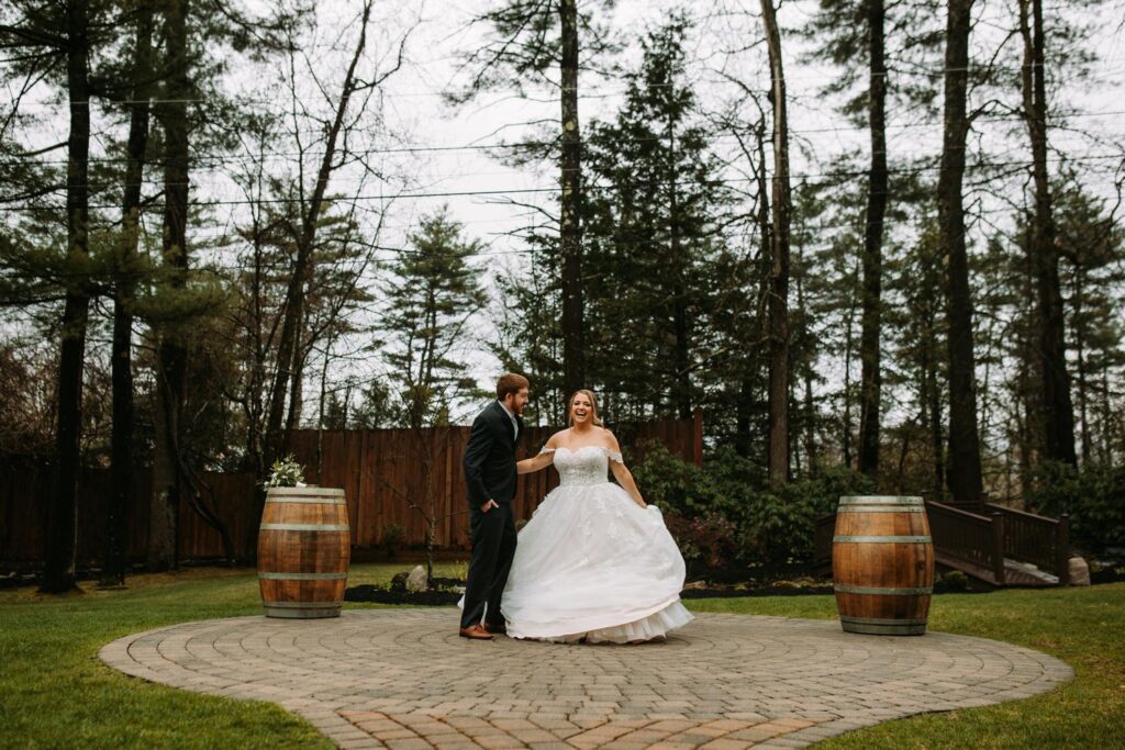 Newlyweds walking hand-in-hand on a garden path beneath tall trees and overcast skies