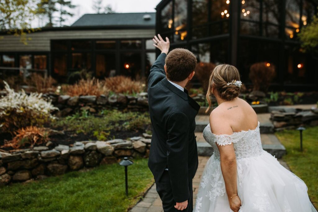 Groom waving to guests while walking with his new bride through the landscaped Birch Wood Vineyards garden