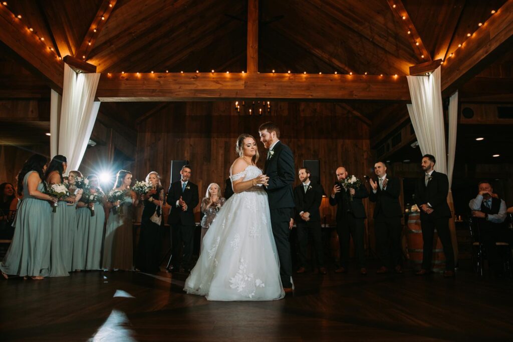 First dance moment under chandeliers as bride and groom share the floor, surrounded by loved ones