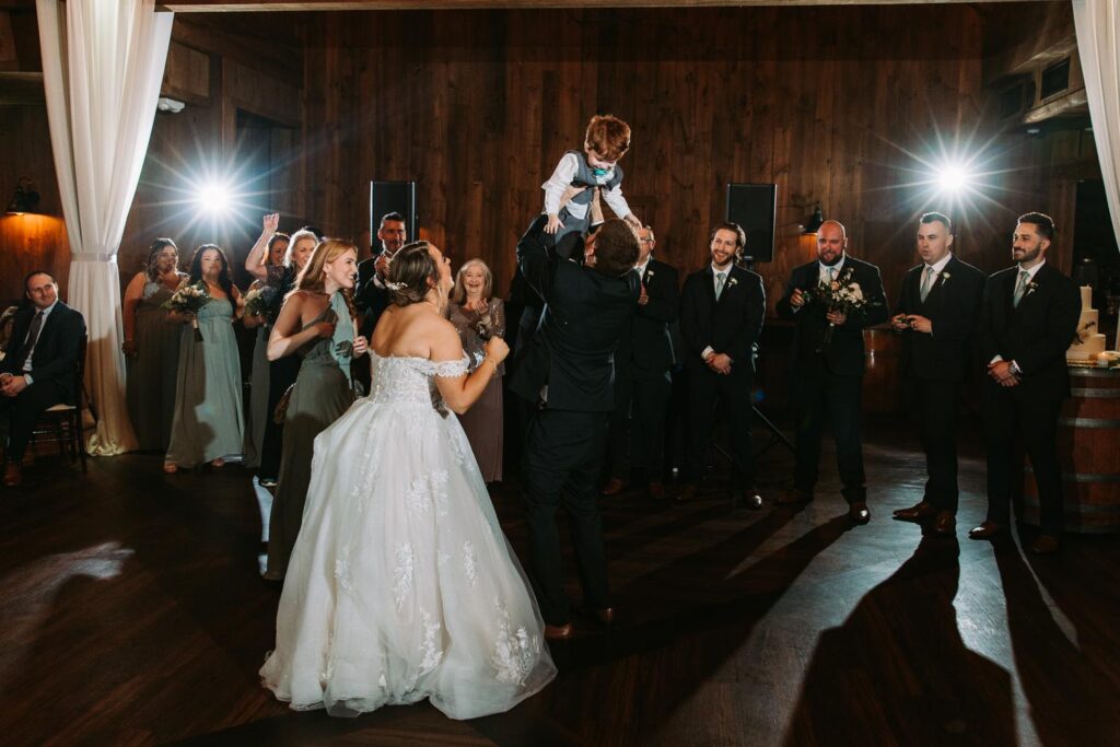 Groom lifting their young son into the air as the crowd cheers and applauds