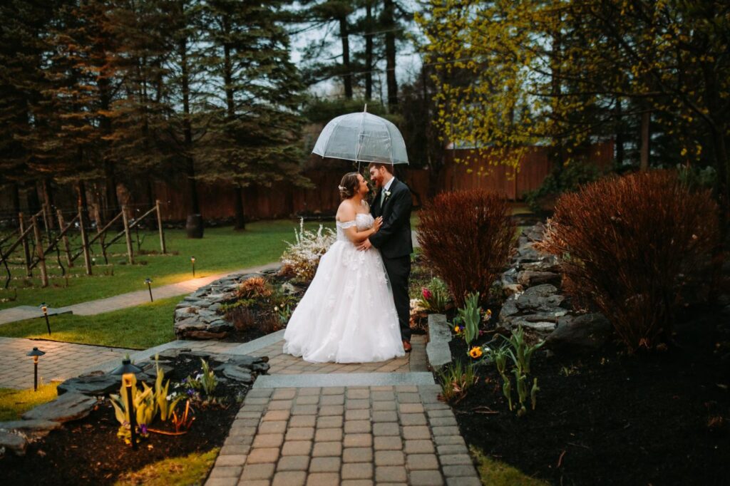 Bride smiling up at groom under a glowing umbrella in the vineyard garden path