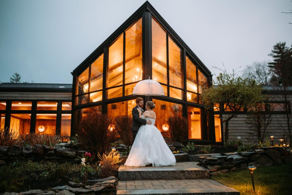Bride standing solo outside the illuminated Birch Wood Vineyards venue at dusk