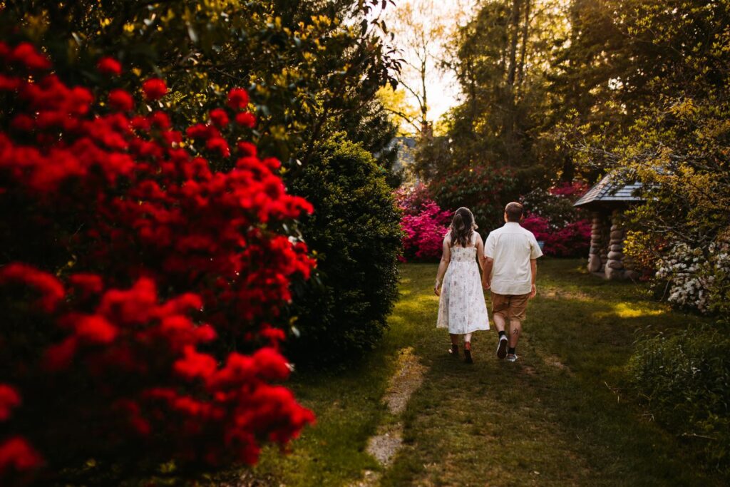 Couple walking away hand in hand down a garden path lined with trees and flowers.