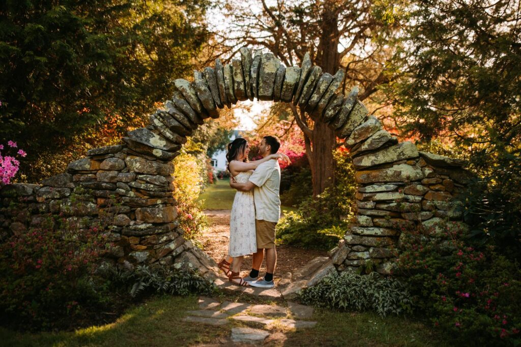 Couple framed by a stone arch, kissing as sunlight streams behind them.