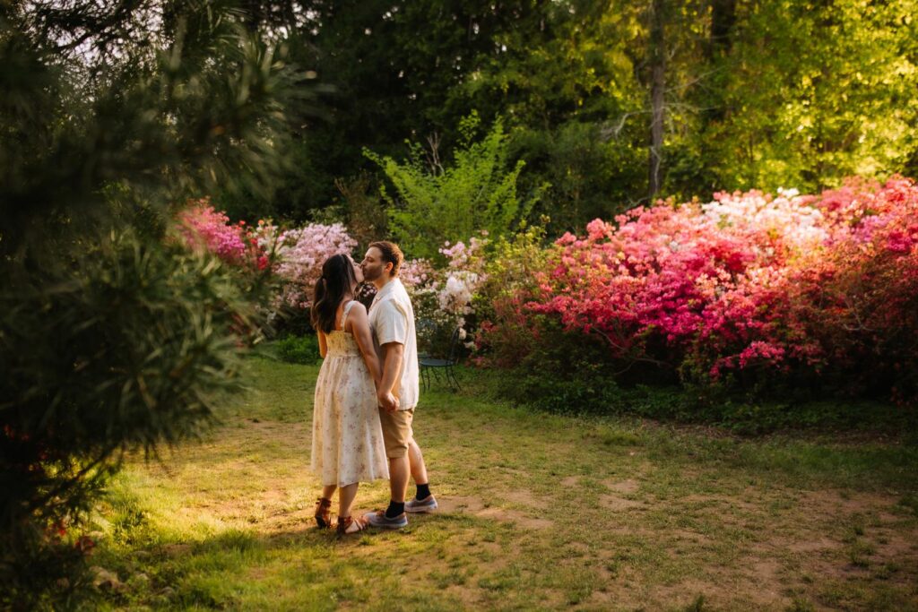Couple standing close in a quiet, shaded spot surrounded by pastel-colored azaleas.