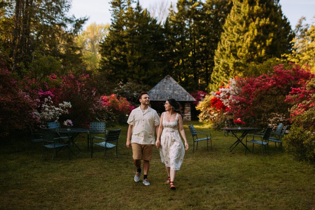 Couple holding hands and walking toward the camera in front of flowering garden shrubs