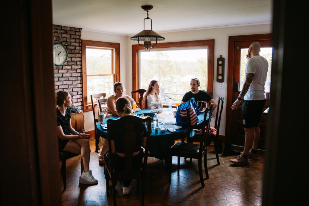 Group of guests chatting around a dining table in a warmly lit farmhouse room