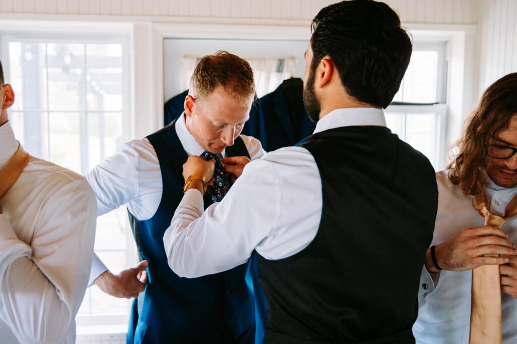 Groom helping groomsman with boutonnière at rustic Catskills wedding venue.