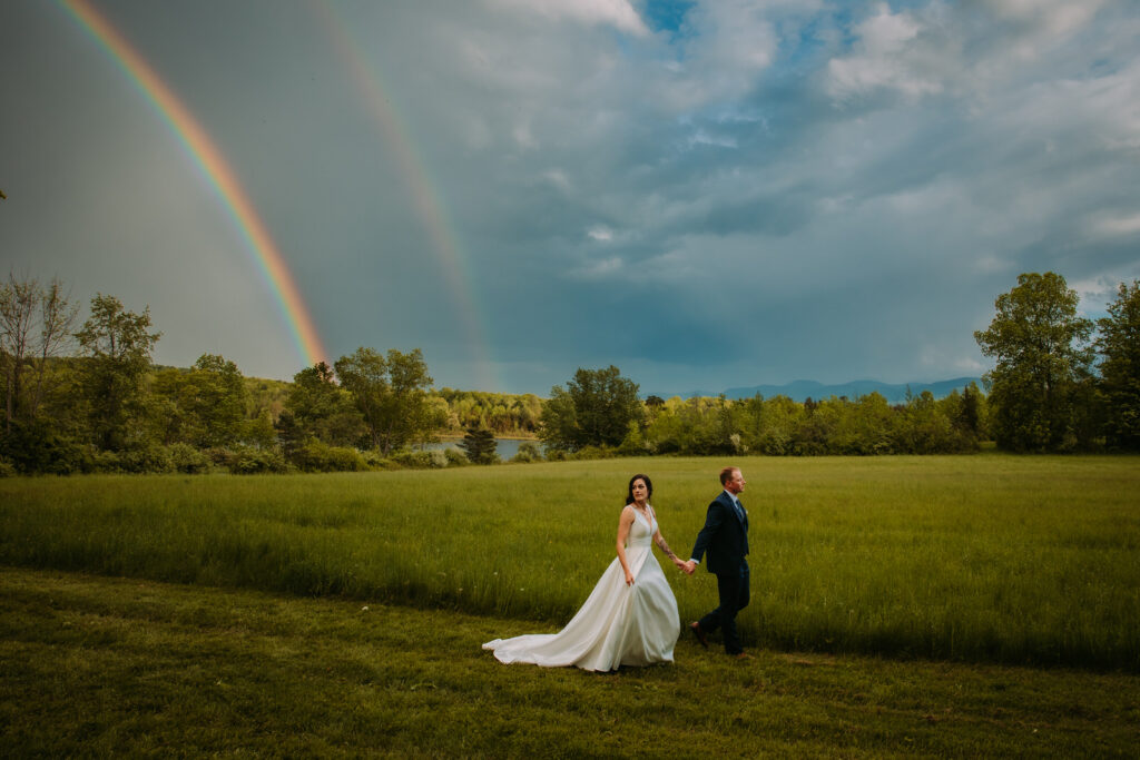 Bride and groom walking in front of a rainbow at Bluebird Farm in Medusa New York