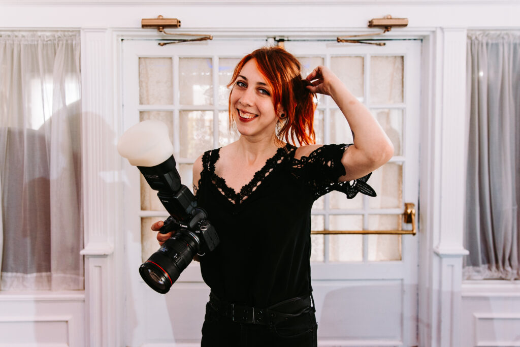 A smiling New England wedding photographer holding a camera