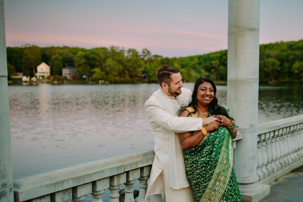 Bride and groom smiling under balcony arch at Grandview Mendon Massachusetts during Indian wedding portraits
