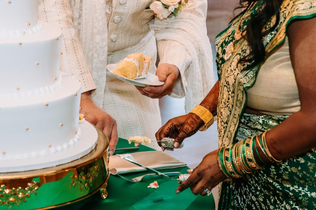 Couple cutting multi-tiered wedding cake at Indian wedding reception inside Grandview Mendon Massachusetts