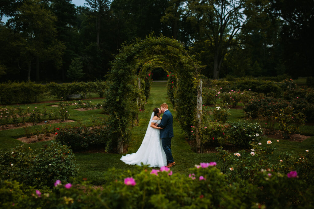 A bride and groom kiss under a rose arch at Elizabeth Park in Hartford, Connecticut at their wedding