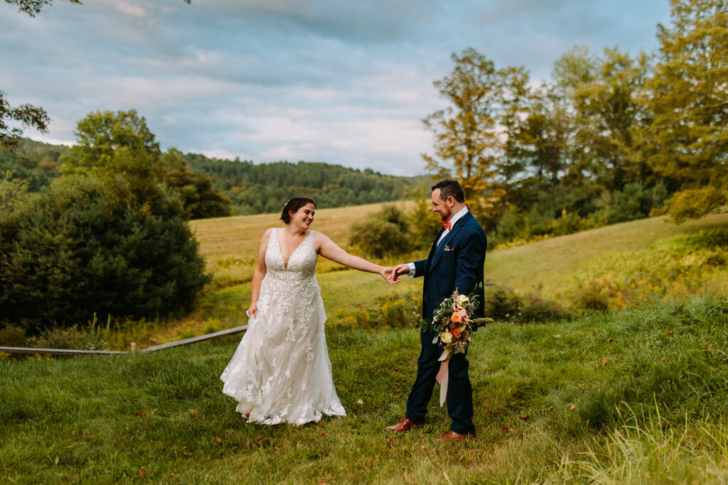 A laughing bride and groom stroll through the hills at the Barn on Gobeille Farms in Sharon, Vermont