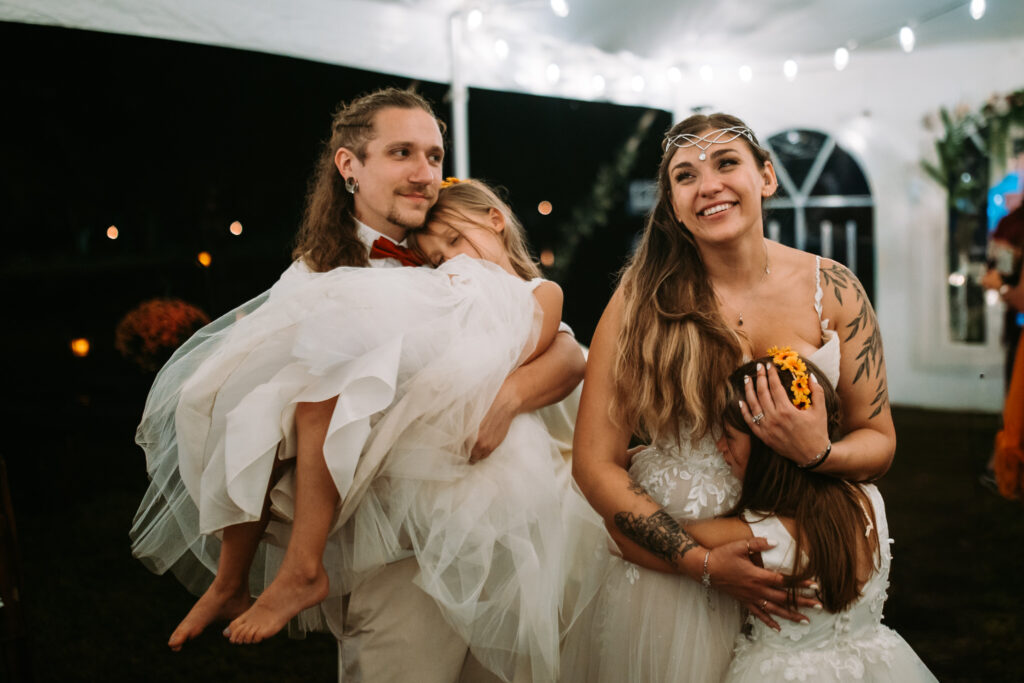 A bride and groom hug their young daughters at their backyard wedding