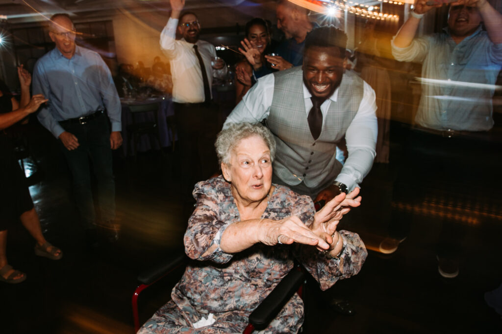 a groom dances with grandmother in a wheelchair at a wedding at Oceanview of Nahant