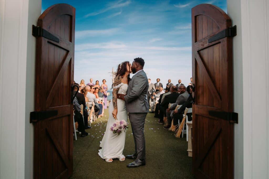 A wedding couple kisses after their wedding ceremony at Oceanview of Nahant, in front of large wooden doors
