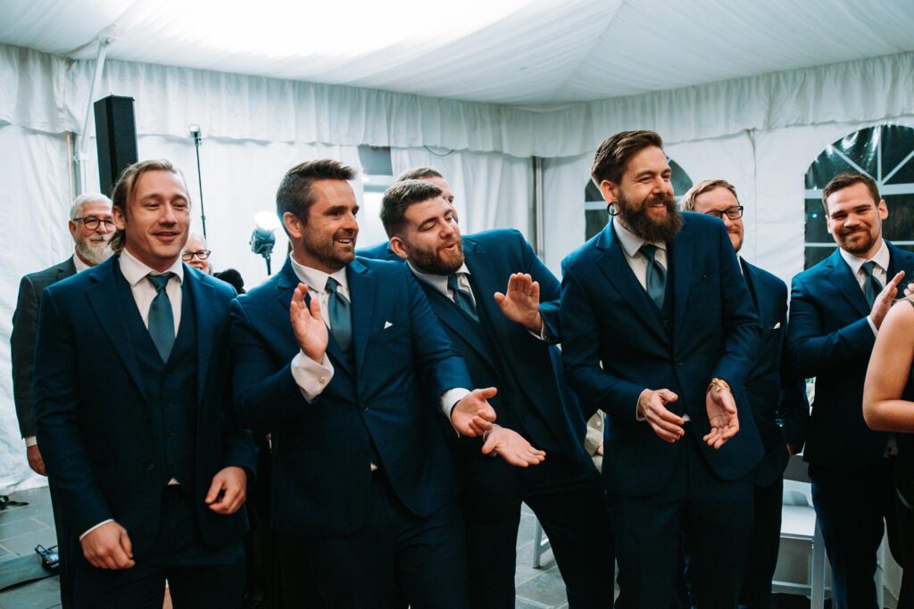 Groomsmen cheering and laughing together inside the reception tent