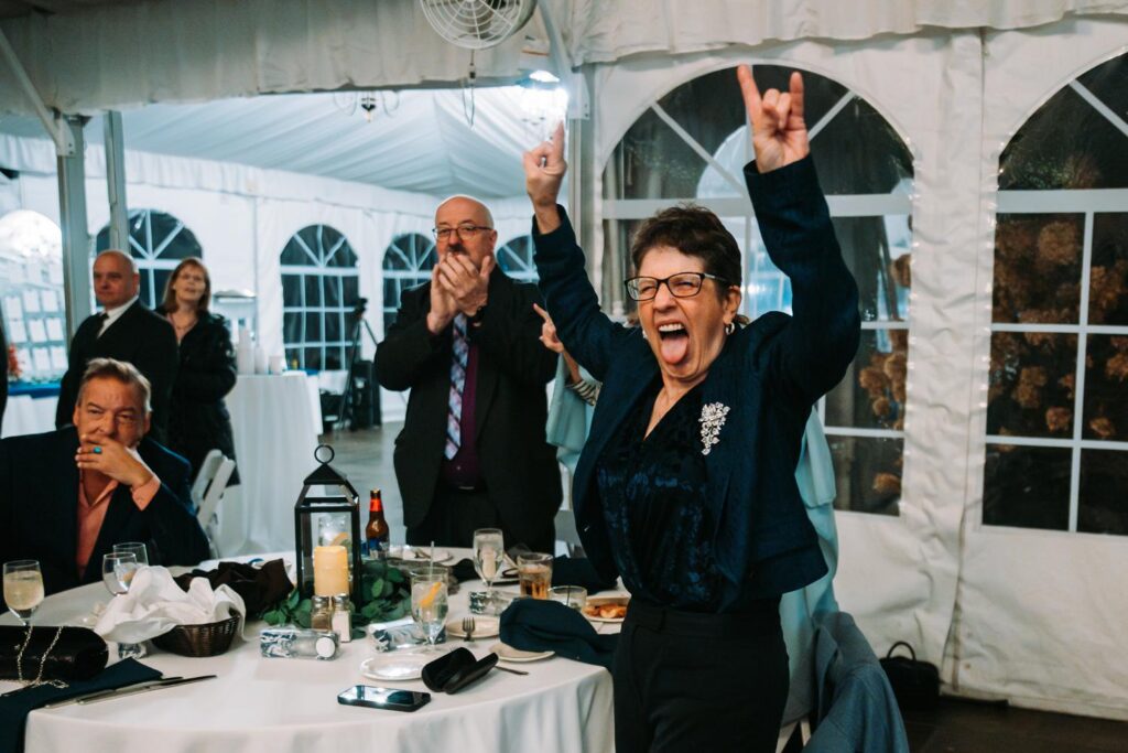Wedding guest throwing up rock hand signs while cheering at a reception table