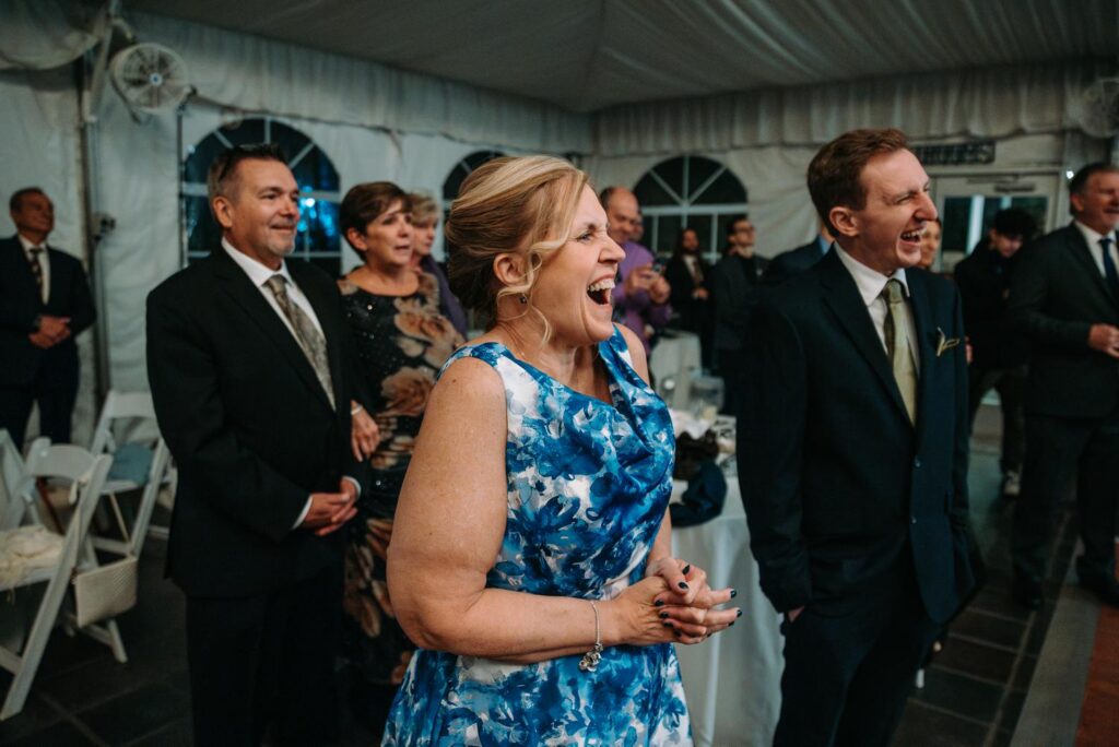 Guests laughing and reacting during speeches inside a tented reception