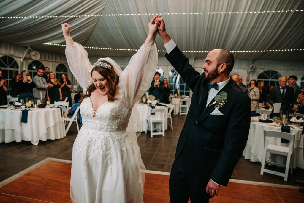 Bride and groom entering the reception tent with guests cheering and raising their arms