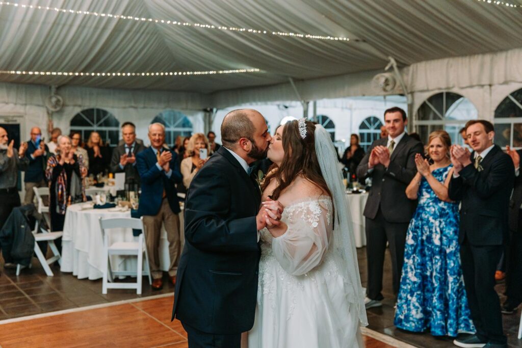 Bride and groom sharing a kiss on the dance floor surrounded by applauding guests