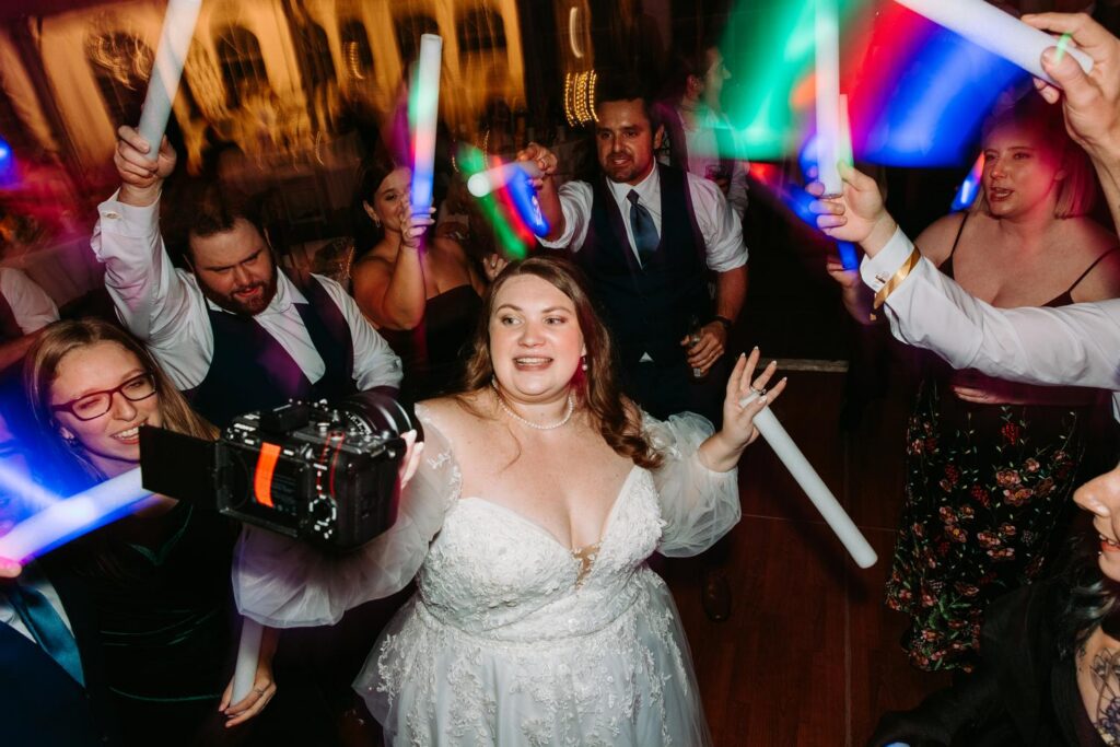 Bride surrounded by guests pointing and cheering during a high-energy dance floor moment
