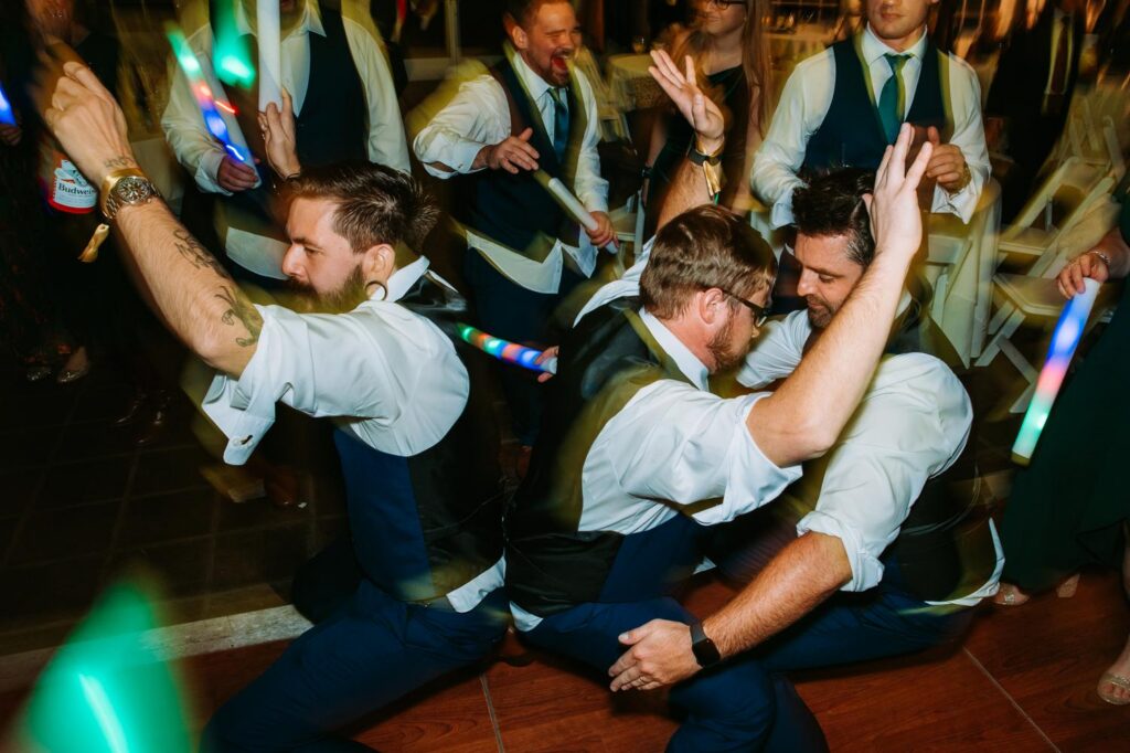 Group of groomsmen dancing energetically together on the reception dance floor