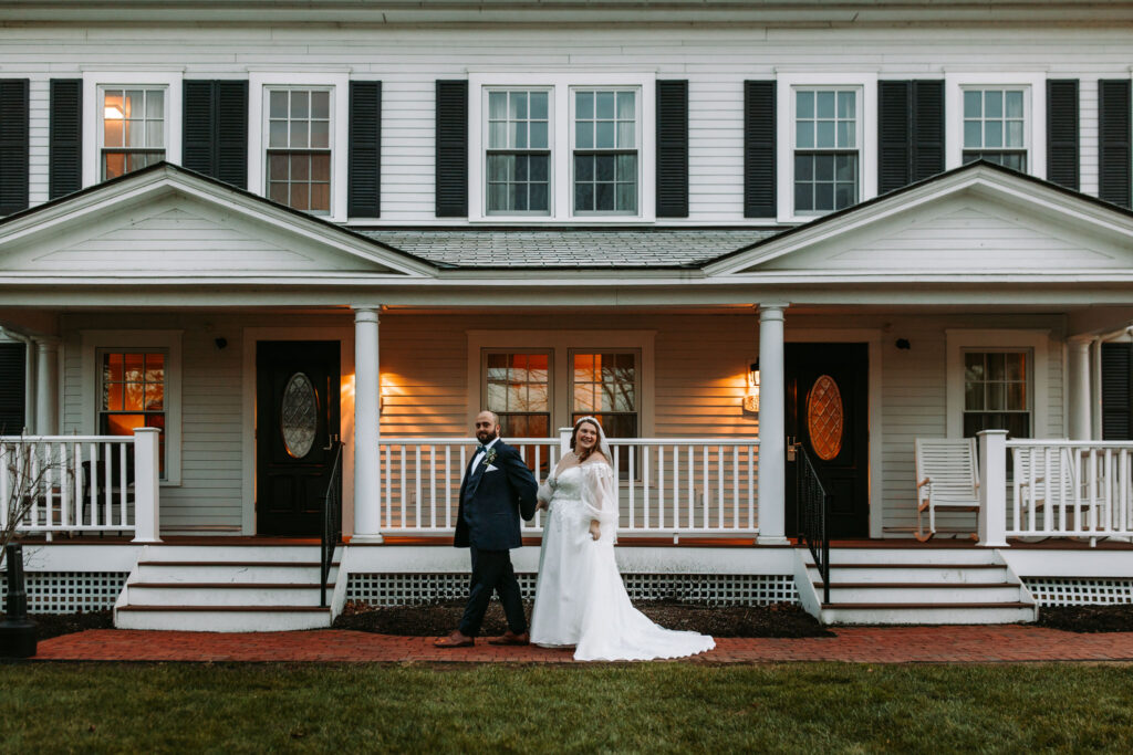 A bride and groom walked hand in hand in front of the house at Publick House in Sturbridge