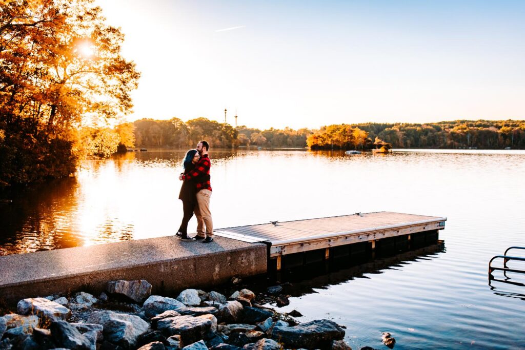 Couple embraces on a dock in the fall at Lincoln Woods State Park during their engagement session