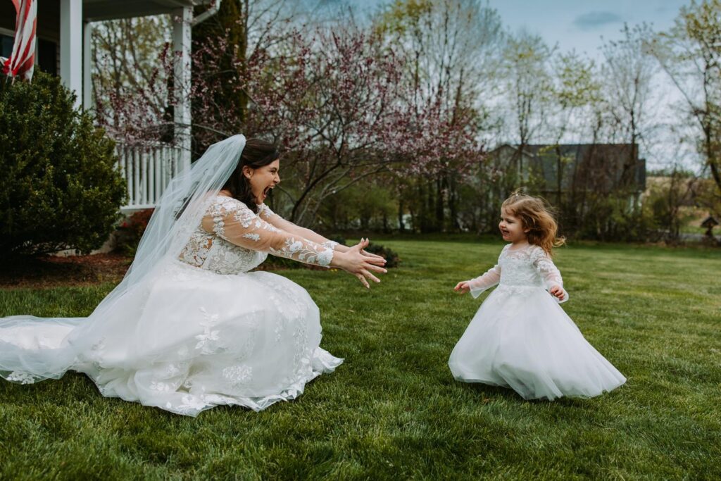 Bride laughing with flower girl on the grass outside before the wedding ceremony