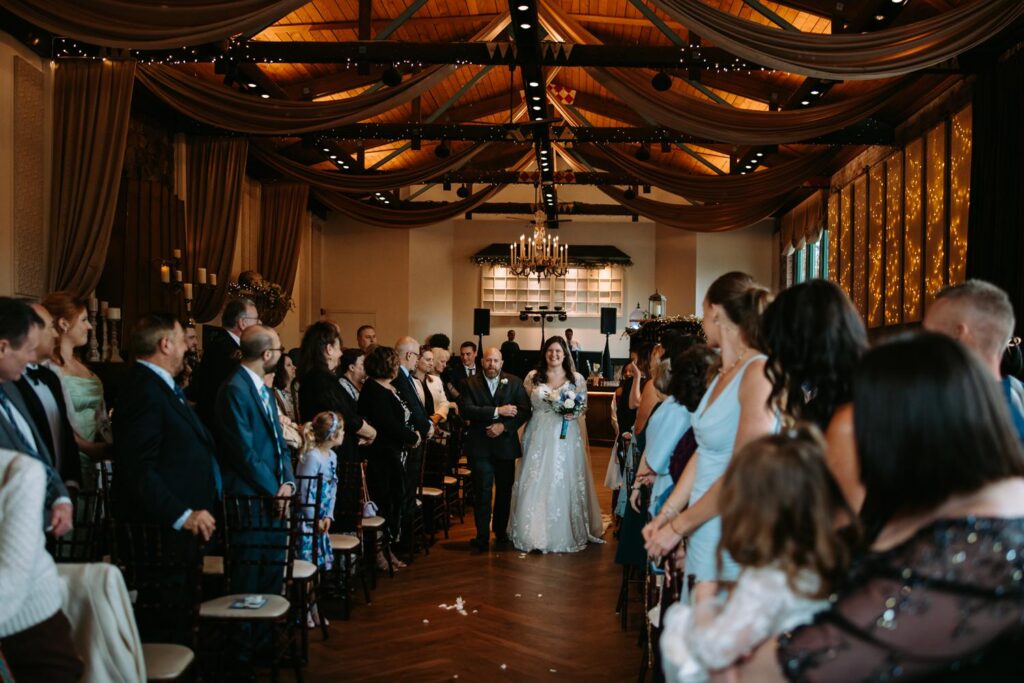 Wide shot of wedding ceremony inside The Pond House Cafe with guests seated and large windows