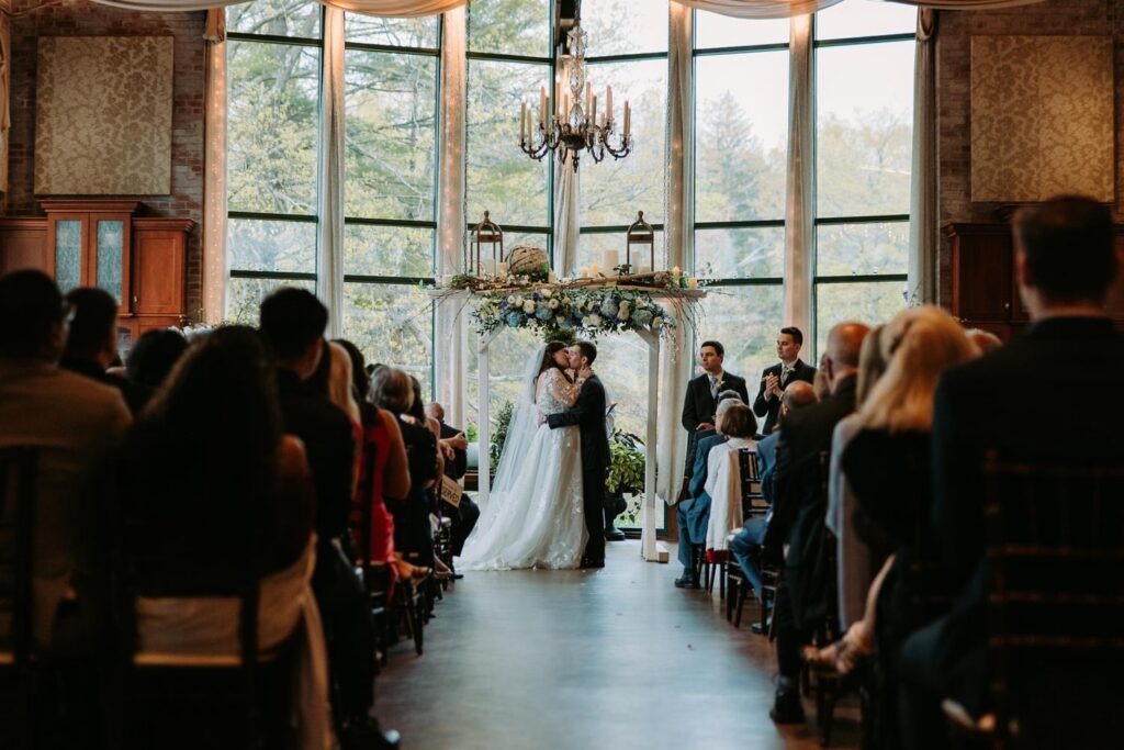 Bride and groom sharing first kiss after ceremony inside The Pond House Cafe reception room