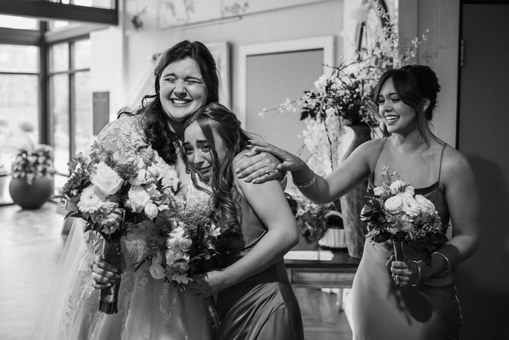 Black and white photo of bride laughing with sisters and bridesmaids in blue dresses